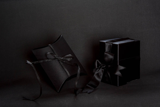 Kaksi mustaa lahjapakkausta, joissa musta nauha rusetti tummalla taustalla, kopioi tilaa. Ystävänpäivä, syntymäpäivä romanttinen konsepti, onnittelukortti
. - Valokuva, kuva