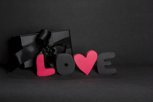 Μαύρο κουτί δώρου και κόκκινα γράμματα Αγάπη σε σκούρο φόντο, αντίγραφο χώρου. Ημέρα του Αγίου Βαλεντίνου, γενέθλια ρομαντική έννοια, ευχετήρια κάρτα. - Φωτογραφία, εικόνα