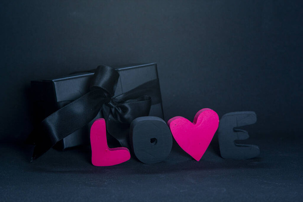 Caja de regalo negro y letras rojas AMOR sobre fondo oscuro, espacio de copia. San Valentín, concepto romántico de cumpleaños, tarjeta de felicitación
. - Foto, imagen