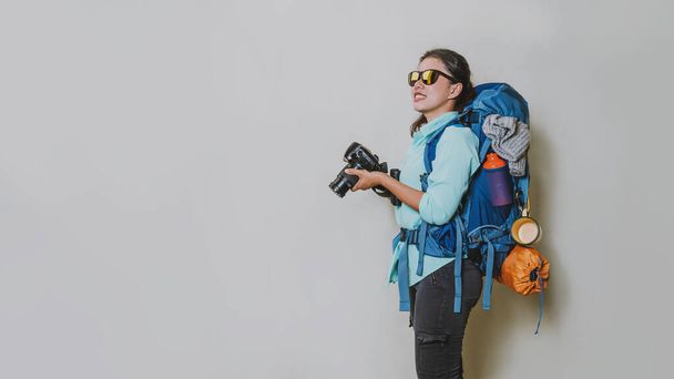 Beyaz bir arka planda el kamerasında sırt çantalı bir kızın resmi. seyahat sırt çantası. - Fotoğraf, Görsel