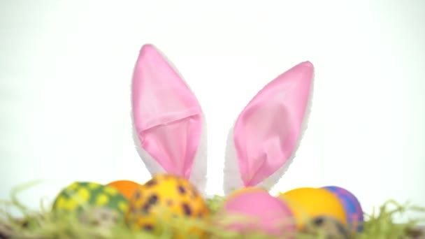 Happy Easter. A man with rabbit ears looks out from behind Easter eggs - Materiał filmowy, wideo