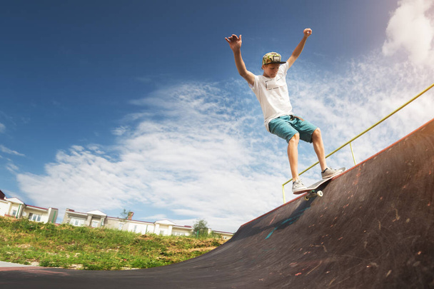 Portrait of a young skateboarder doing a trick on his skateboard on a halfpipe ramp in a skate park in the summer on a sunny day. The concept of youth culture of leisure and sports - Zdjęcie, obraz