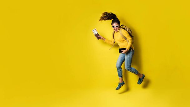 Woman traveler with suitcase, holding passport with ticket on Yellow background. - Фото, зображення