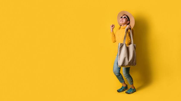 Portré egy izgatott, gyönyörű lányról, aki ruhát és napszemüveget visel, bevásárlószatyrokkal a kezében. Vidám fiatal nő táska sárga háttér. - Fotó, kép