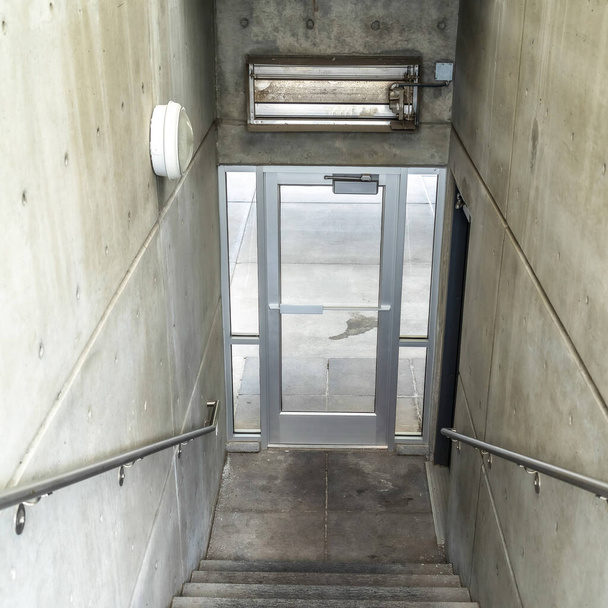 Kwadratowa klatka schodowa wewnątrz budynku schodzącego do szklanych drzwi prowadzących na zewnątrz - Zdjęcie, obraz