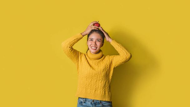 Jovencita alegre sobre fondo amarillo en el estudio. Una chica sonriente y feliz con una manzana apoyada en su cabeza. El concepto de ejercicio para una buena salud
. - Foto, Imagen