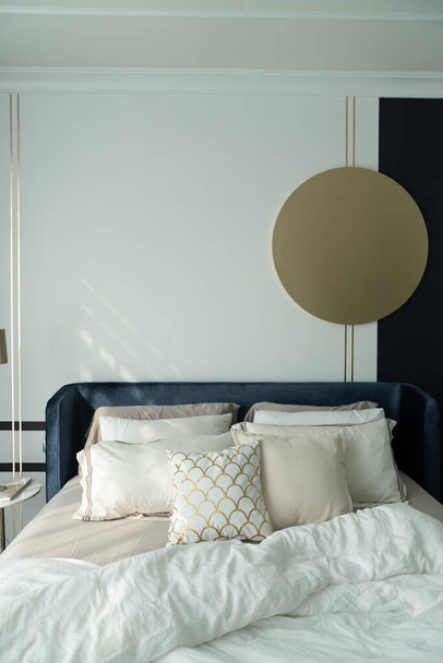 丸みを帯びた大理石のナイトテーブルと背景/居心地の良いインテリアデザインのネイビーブルーのペンキの壁で飾られた柔らかい枕の設定を持つベッドルームの角のネイビーブルーベルベットのベッド - 写真・画像