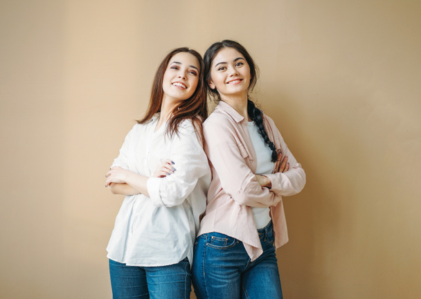 Jeune brune insouciante souriante filles amis sœurs en chemises décontractées et jeans isolés sur fond beige
 - Photo, image