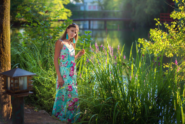 Full-length portrait of a beautiful girl near a lake with tall grass. Summer walk. Long floor vlate - Foto, Imagem
