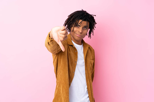 Młody Afroamerykanin w sztruksowej kurtce na odizolowanym różowym tle pokazuje kciuk w dół z negatywnym wyrazem - Zdjęcie, obraz