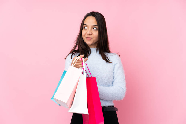 Junge Frau mit Einkaufstasche vor isoliertem rosa Hintergrund intrigiert etwas - Foto, Bild