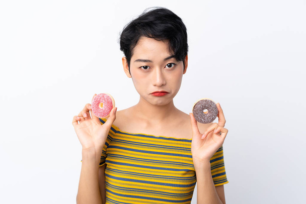 Joven chica asiática sosteniendo donuts con expresión triste
 - Foto, imagen