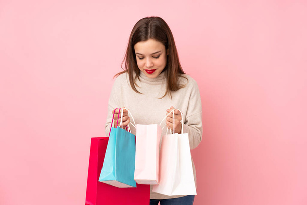 Adolescente menina isolada no fundo rosa segurando sacos de compras e olhando dentro dele
 - Foto, Imagem