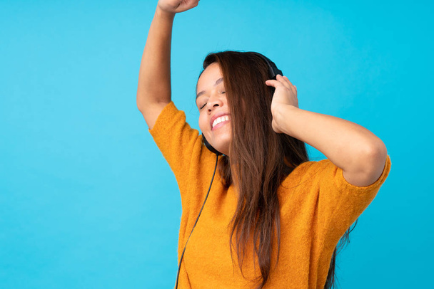 Νεαρή γυναίκα ακούει μουσική πάνω από απομονωμένο μπλε τοίχο - Φωτογραφία, εικόνα