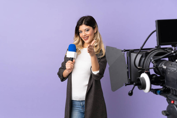 Riporter tinédzser lány kezében egy mikrofon és riport hírek elszigetelt lila háttér rázza kezét lezárása egy jó üzlet - Fotó, kép