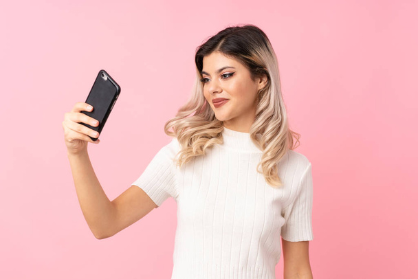 Adolescente sur fond rose isolé prenant un selfie avec le mobile
 - Photo, image