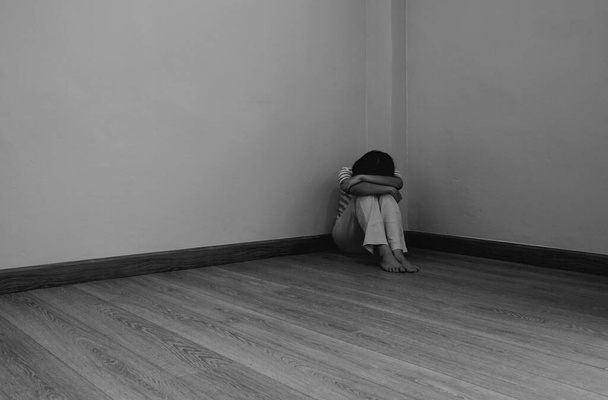 Młoda smutna kobieta z depresyjnym humorem siedząca w rogu pokoju. czerń i biel - Zdjęcie, obraz