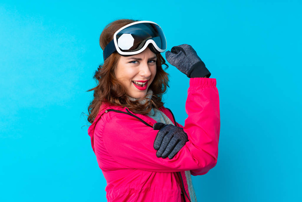 Gözlüklü kayakçı kadın mavi duvarın üstünde güçlü bir jest yapıyor. - Fotoğraf, Görsel