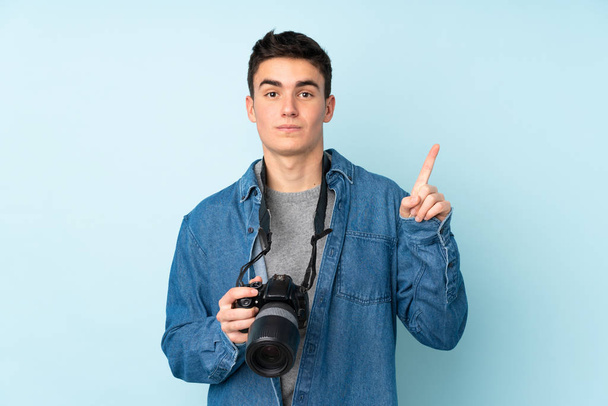 Tiener fotograaf man geïsoleerd op blauwe achtergrond wijzen met de wijsvinger een geweldig idee - Foto, afbeelding