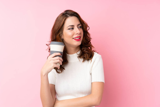 Young Russian woman over isolated pink background holding coffee to take away - Photo, Image