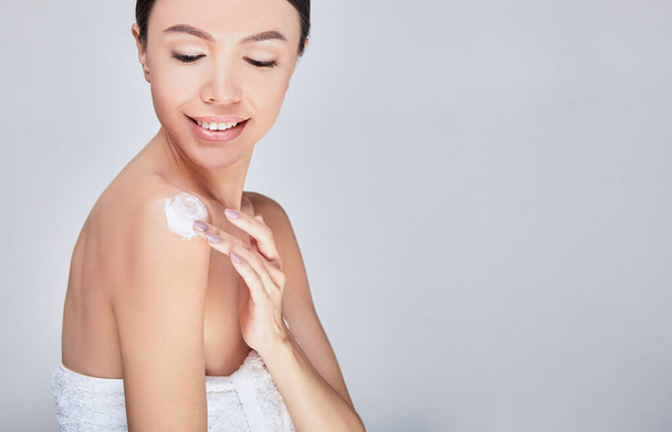 A young Asian woman puts body cream on her bare shoulder. - Fotó, kép