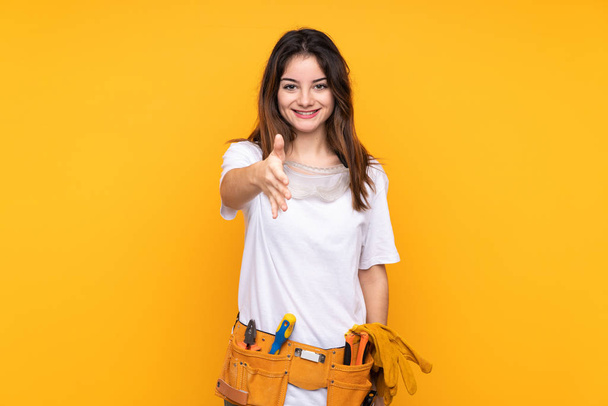 Joven electricista mujer sobre aislado en fondo amarillo apretón de manos después de buen trato
 - Foto, imagen