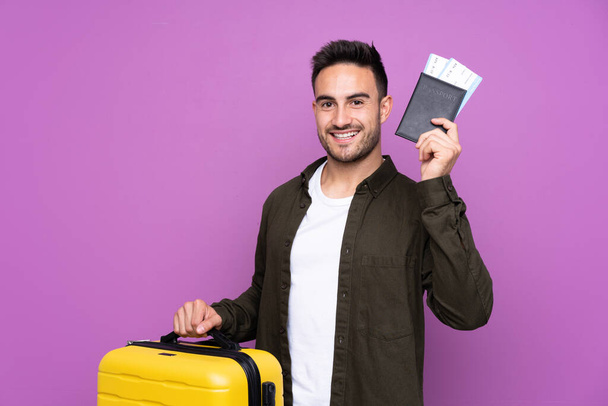 Jeune homme beau sur fond violet isolé en vacances avec valise et passeport
 - Photo, image