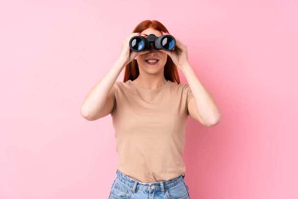 Young redhead woman over isolated pink background with black binoculars - Photo, Image