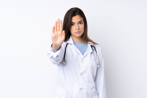 Teenager girl over isolated white background wearing a doctor gown and making stop sign - Фото, зображення