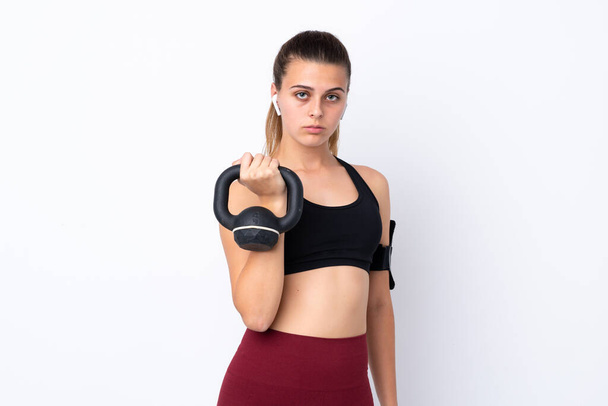 Adolescente chica deportiva sobre fondo blanco aislado haciendo levantamiento de pesas con kettlebell y mirando hacia el frente
 - Foto, Imagen