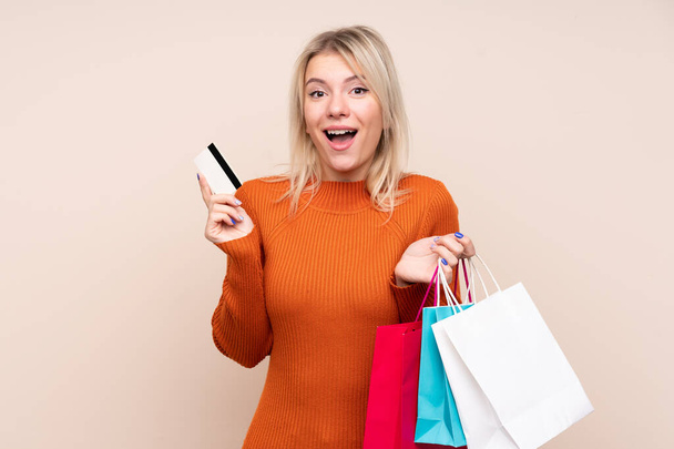 Young blonde woman over isolated background holding shopping bags and surprised - Photo, Image
