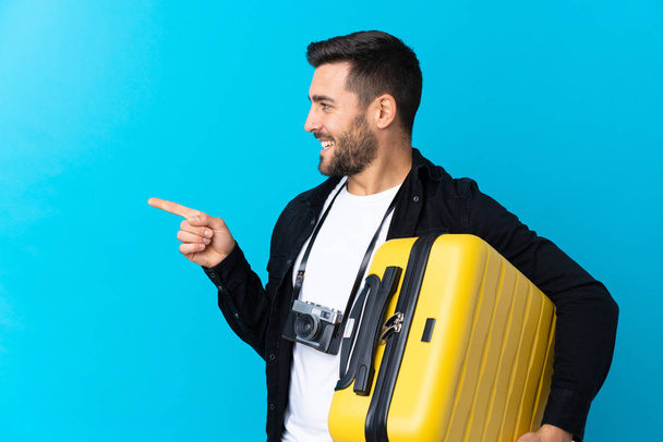 Voyageur tenant une valise sur fond bleu isolé pointant vers le côté pour présenter un produit
 - Photo, image