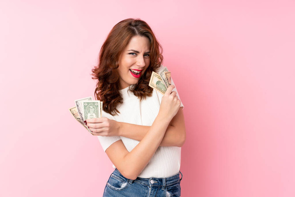 Young Russian woman over isolated pink background taking a lot of money - Fotó, kép