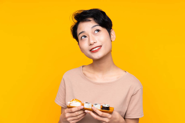 jong aziatisch meisje met sushi op zoek omhoog terwijl glimlachen - Foto, afbeelding
