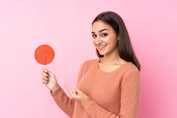 Young girl holding a lollipop over pink background and pointing it - Photo, image