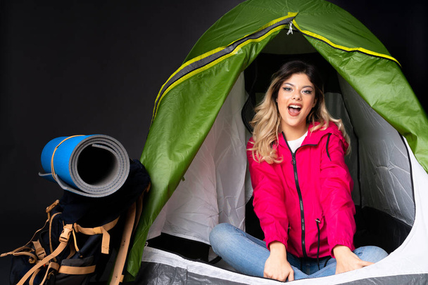 Подросток внутри кемпинга зеленая палатка изолированы на черном фоне с удивлением выражение лица - Фото, изображение