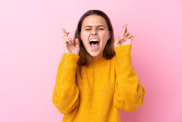 Teenager girl with yellow sweater over isolated pink background with fingers crossing - Photo, Image