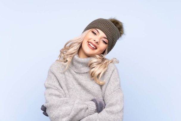 Young teenager girl with winter hat over isolated blue background laughing - Zdjęcie, obraz