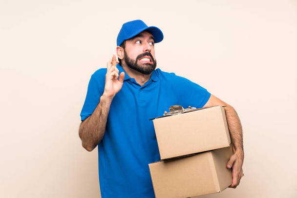 Delivery man with beard over isolated background with fingers crossing and wishing the best - Фото, зображення
