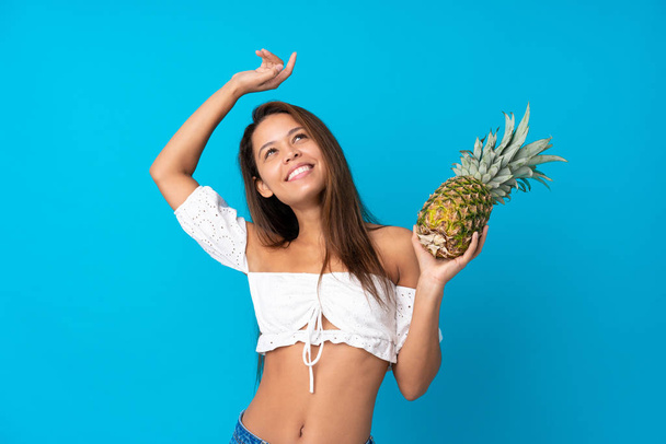 Jonge vrouw in de zomervakantie met ananas over geïsoleerde blauwe achtergrond - Foto, afbeelding