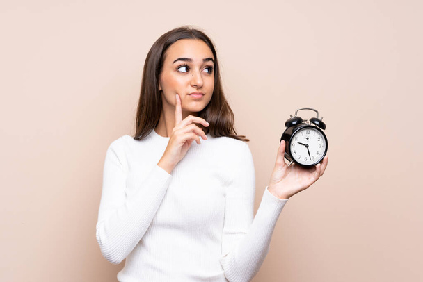 Young woman over isolated background holding vintage alarm clock - Фото, изображение