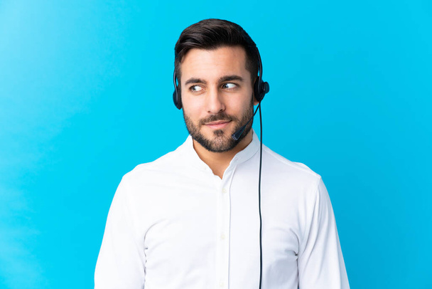 Uomo telemarketer che lavora con un auricolare su isolato sfondo blu in piedi e guardando lateralmente
 - Foto, immagini