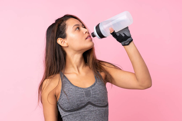 Jeune fille brésilienne sport sur fond rose isolé avec bouteille d'eau de sport - Photo, image