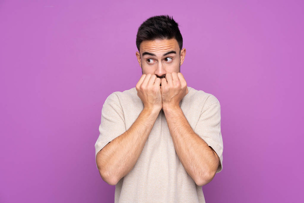 Mladý pohledný muž přes izolované fialové pozadí nervózní a strach dávat ruce k ústům - Fotografie, Obrázek