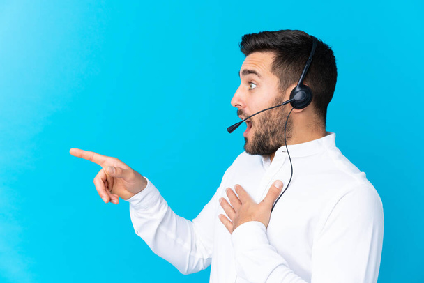 Hombre de telemarketer trabajando con un auricular sobre un fondo azul aislado apuntando con el dedo hacia un lado
 - Foto, imagen