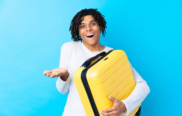 Young African American traveler man holding a suitcase with shocked facial expression - Foto, Imagen