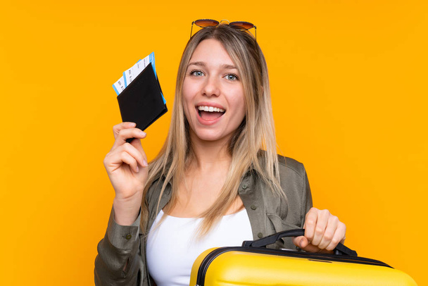 Młoda blondynka na odizolowanym żółtym tle na wakacjach z walizką i paszportem - Zdjęcie, obraz