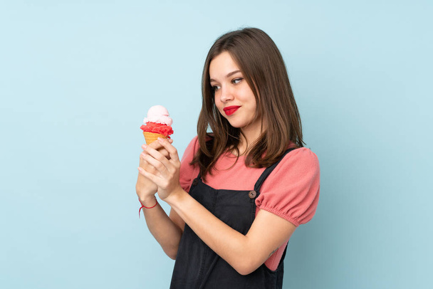 Девочка-подросток держит корнет мороженое изолировано на синем фоне - Фото, изображение