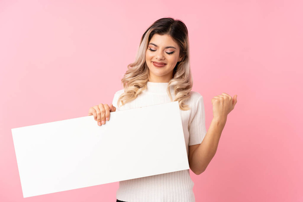 Teenager girl over isolated pink background holding an empty white placard for insert a concept - Photo, Image