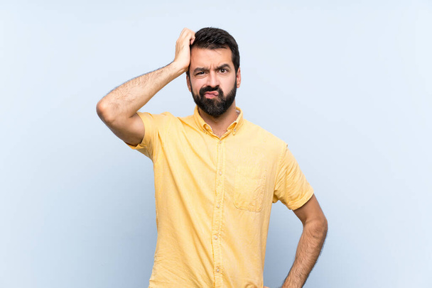 Jovem com barba sobre fundo azul isolado com uma expressão de frustração e não compreensão
 - Foto, Imagem